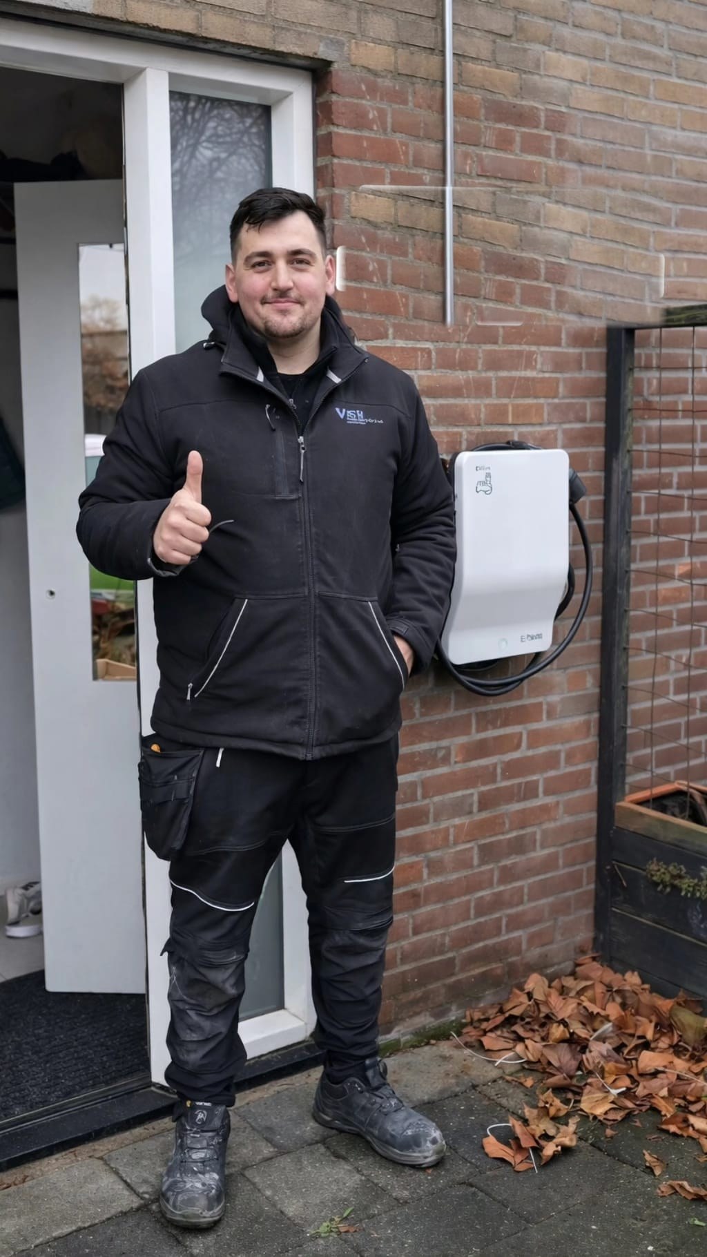 Monteur van Volta Elektrotechniek steekt zijn duim op naast een zojuist gemonteerde wandlader aan een woning